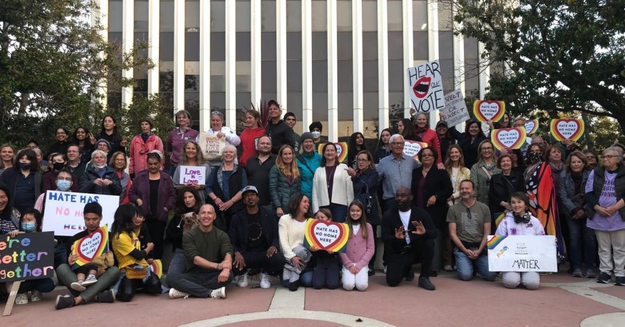 Community members hold signs with supporting messages for LGBTQ+ community